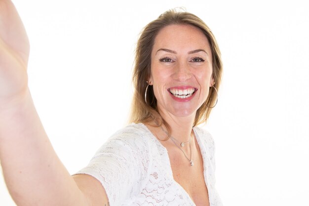 La bella donna bionda abbastanza rende il telefono della macchina fotografica del selfie più isolato su bianco