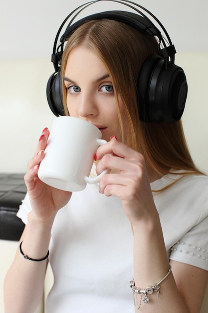 La bella donna bionda ascolta la musica sulla musica delle cuffie di grandi dimensioni e beve una tazza di caffè