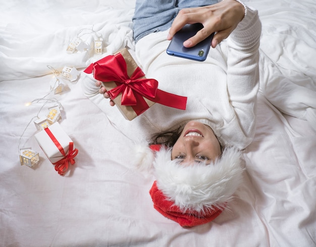 La bella donna castana felice fa un selfie per telefono in un maglione bianco e un cappello di Natale e