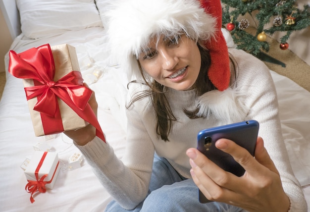 La bella donna castana felice fa un selfie per telefono in un maglione bianco e un cappello di Natale e
