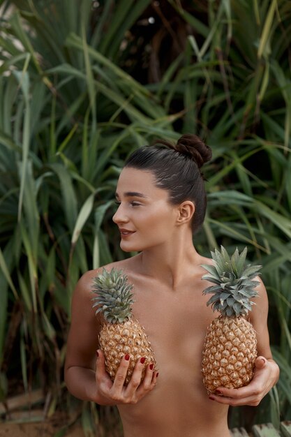 La bella donna con l'abbronzatura bronzea tiene gli ananas nelle mani