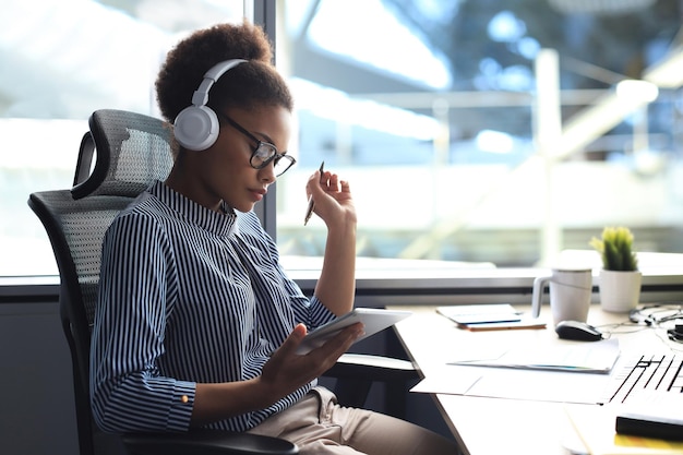 La bella donna d'affari afroamericana sta lavorando utilizzando la tavoletta digitale mentre è seduto in un ufficio creativo