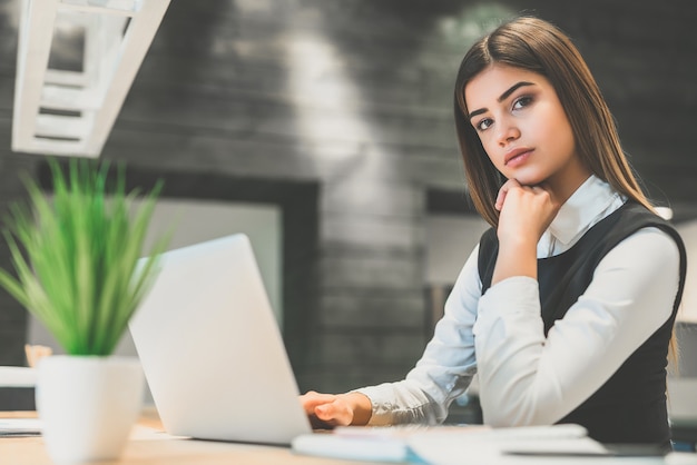 La bella donna d'affari con un laptop seduto al desktop