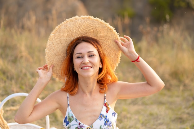 La bella donna dai capelli rossi gode del tramonto sulla natura. Pic-nic in campo.