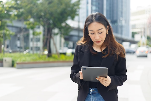 La bella donna di affari asiatica indossa il vestito nero facendo uso della compressa fuori dall'ufficio. donna freelance stile di vita umano urbano. Lavoro in linea. copia spazio per la parola di testo.