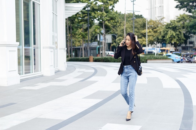 La bella donna di affari asiatica indossa un abito nero che parla al telefono a piedi per una strada cittadina. copia uso dello spazio per la parola di testo.