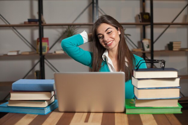 La bella donna è felice del suo lavoro di successo con il laptop grigio e i suoi libri al tavolo di legno