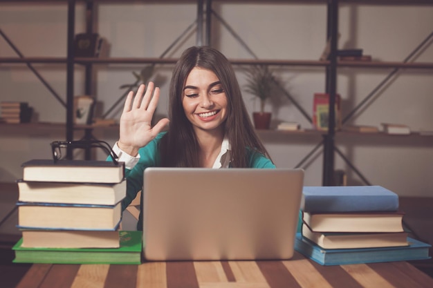 La bella donna è felice del suo lavoro di successo con laptop grigio e libri al tavolo di legno