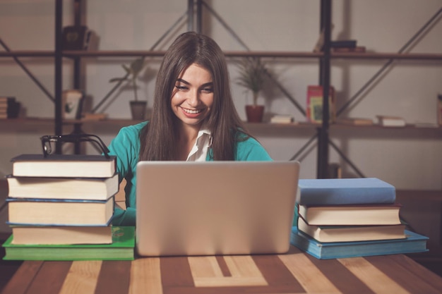 La bella donna è felice del suo lavoro di successo con laptop grigio e libri al tavolo