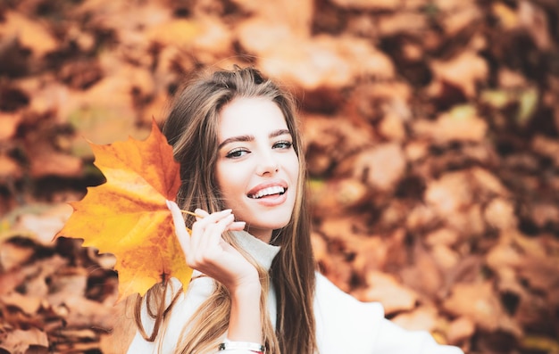 La bella donna felice con un sorriso tiene una foglia gialla di autunno vicino al fronte