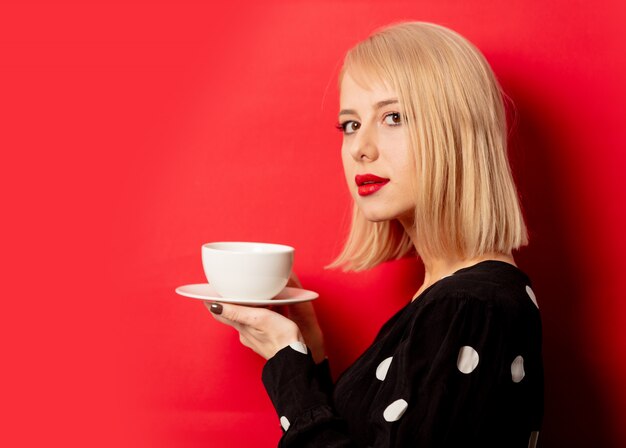 La bella donna francese tiene la tazza di caffè sulla parete rossa