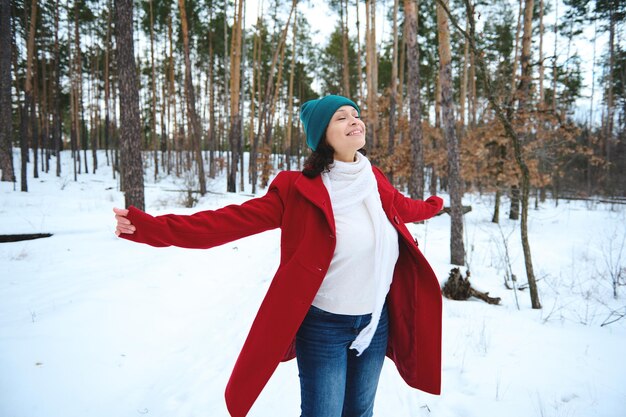 La bella donna gode di una bella giornata di sole mentre ci si rilassa in una natura innevata I raggi del sole cadono attraverso i pini su un sentiero nel bosco innevato Vacanze invernali e concetto di viaggio Attività ricreative all'aperto