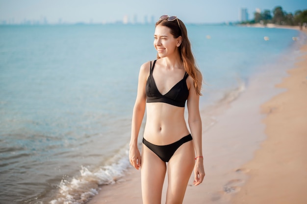 La bella donna in bikini nero sta camminando sulla spiaggia