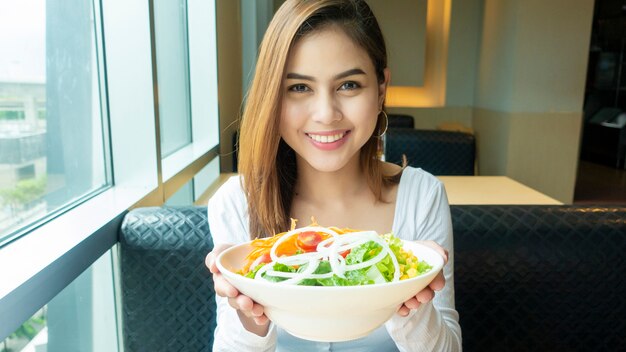 La bella donna in buona salute sta tenendo l'insalata delle verdure