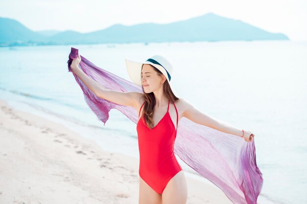 La bella donna in costume da bagno rosso sta rilassandosi sulla spiaggia, concetto dell&#39;estate
