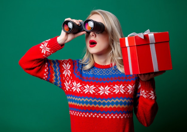 La bella donna in maglione di Natale tiene il contenitore di regalo e il binocolo