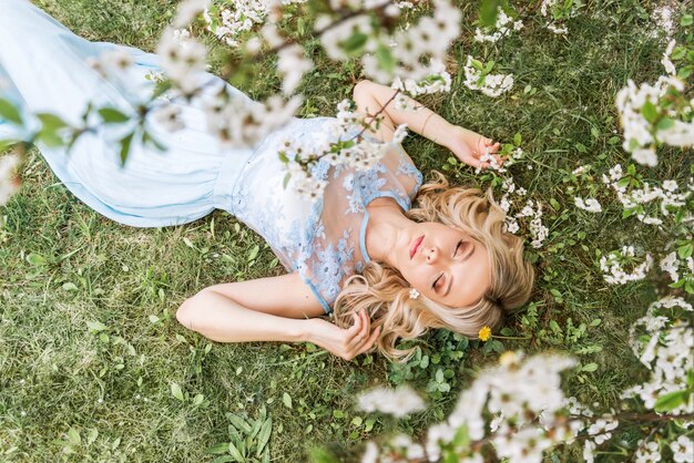 La bella donna in un vestito lungo sta trovandosi sull'erba in un giardino della molla