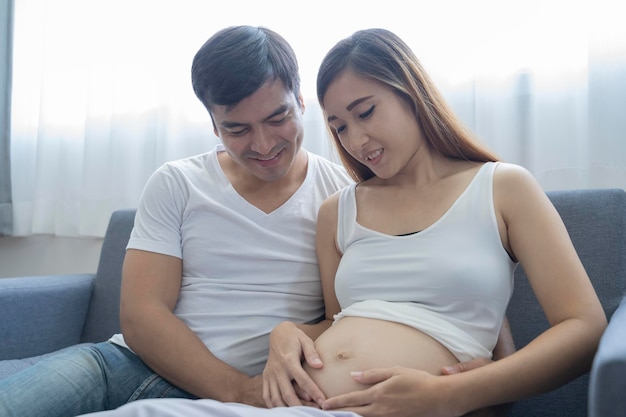 La bella donna incinta e il suo bel marito sorridono mentre trascorrono del tempo insieme sul divano