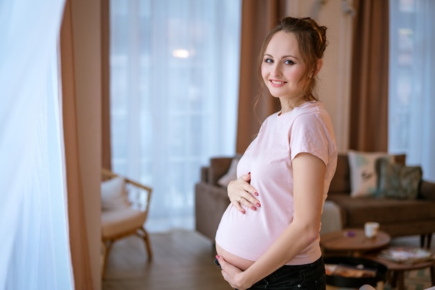 La bella donna incinta felice sta alla finestra