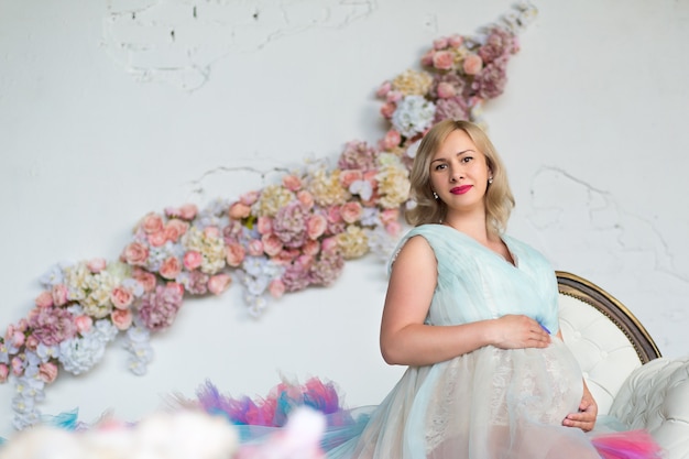 La bella donna incinta in un vestito gonfio colorato è seduta in uno studio floreale con copyspace