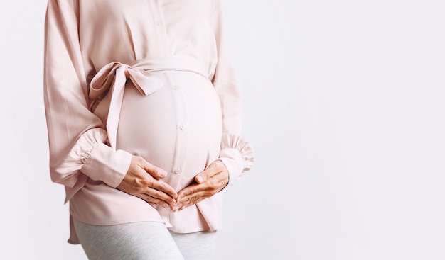 La bella donna incinta si tiene per mano sulla pancia su fondo bianco