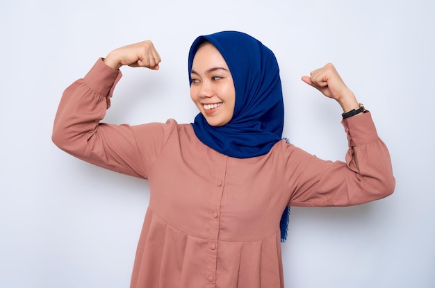 La bella donna musulmana asiatica sorridente in camicia rosa alza le braccia e mostra i bicipiti hanno dimostrato il suo successo dopo l'allenamento in una palestra isolata su sfondo bianco Concetto di stile di vita religioso della gente