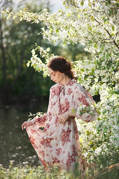 La bella donna romantica sta in rami di melo in fiore. Ritratto di primavera ragazza in fiori melo