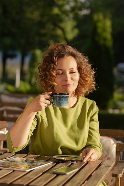 La bella donna seduta in un caffè estivo a bere il caffè