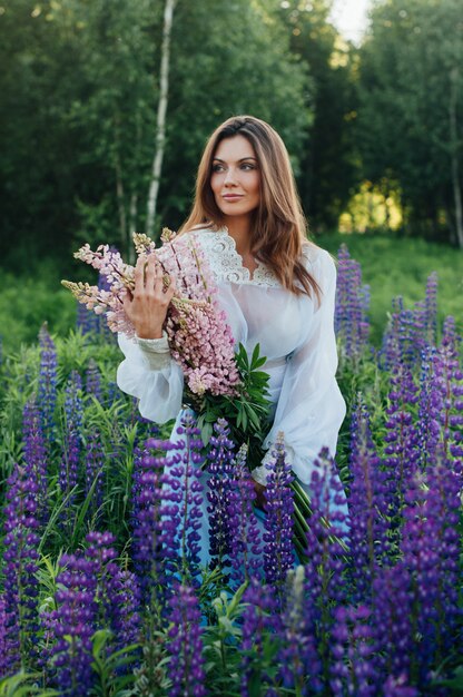 La bella donna si è vestita in un vestito nei lupini dei fiori al tramonto