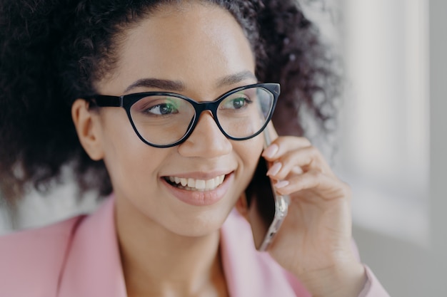 La bella donna sorridente indossa i vetri ottici e tiene il telefono cellulare moderno