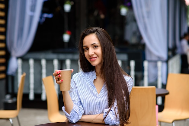 La bella donna sta bevendo il caffè in un caffè della via.