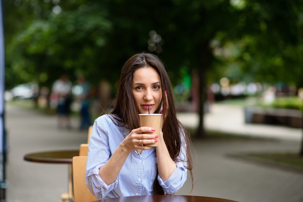 La bella donna sta bevendo il caffè in un caffè della via.