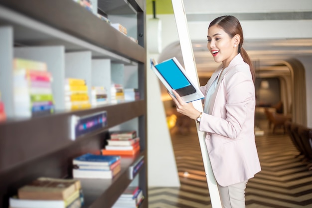 La bella donna sta leggendo i libri in biblioteca