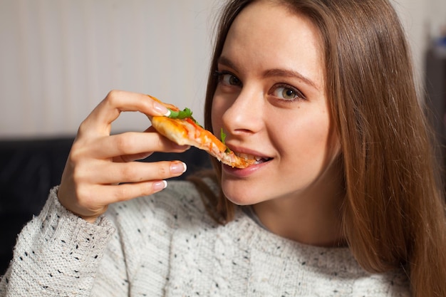 La bella donna sta mangiando una fetta di pizza