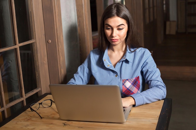 La bella donna sta scrivendo sul computer portatile al tavolo