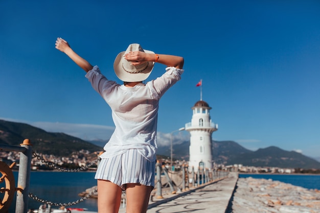 La bella donna sta vicino al faro in una camicia bianca e un cappello di paglia