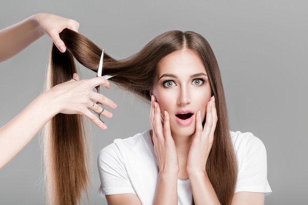 La bella donna stupita con i capelli lunghi lisci tiene le forbici per l'acconciatura