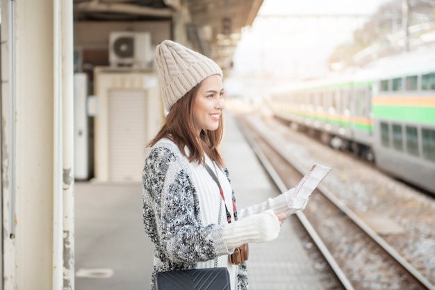 La bella donna turistica sta stando sulla piattaforma ferroviaria con la sua mappa