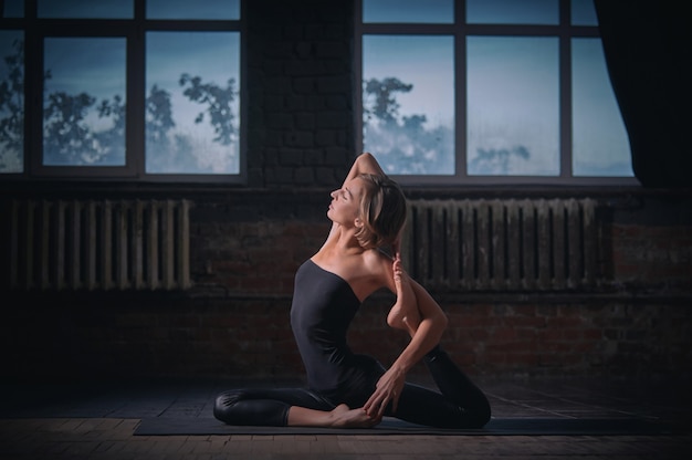 La bella donna yogini in forma sportiva pratica l'asana yoga Eka Pada Rajakapotasana nella sala buia