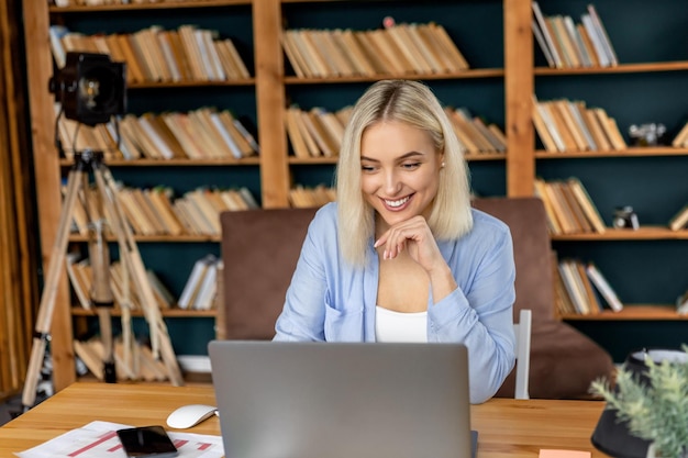 La bella e allegra freelance femminile sta usando il laptop per una riunione video con i colleghi