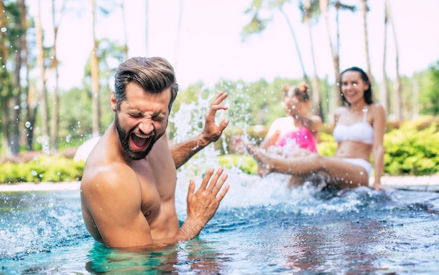 La bella famiglia moderna eccitata e felice si diverte in piscina durante le vacanze estive.