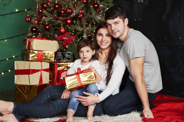 La bella famiglia si siede vicino all'albero di Natale con scatole regalo la sera d'inverno, godendosi il tempo trascorso insieme.