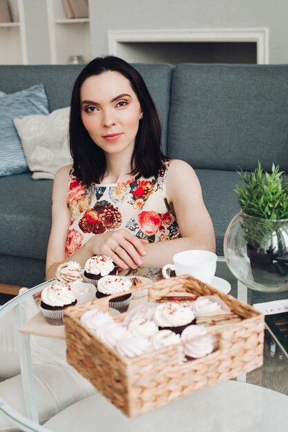 La bella femmina caucasica con i capelli scuri corti fa colazione con dolci, marshmallow e biscotti