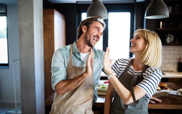 La bella giovane coppia adorabile sta sorridendo mentre cucina insieme nella cucina a casa