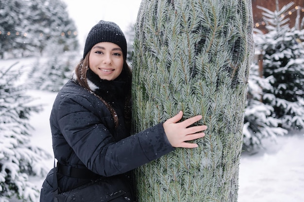 La bella giovane donna abbraccia il suo albero di natale donna felice in previsione della festa