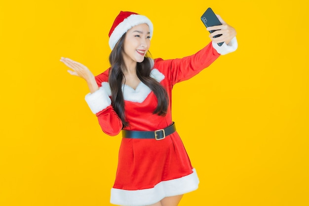 La bella giovane donna asiatica del ritratto indossa il costume di natale con il telefono cellulare su yellow