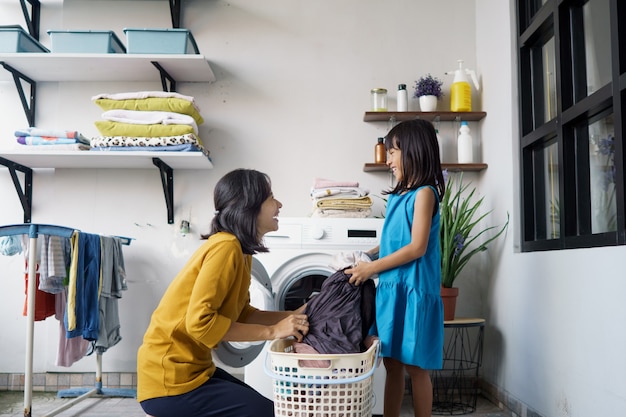 La bella giovane donna asiatica e il piccolo aiutante della ragazza del bambino stanno facendo il bucato a casa.