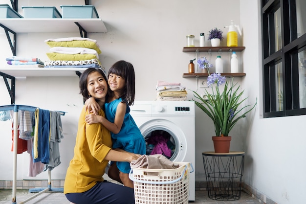La bella giovane donna asiatica e il piccolo aiutante della ragazza del bambino stanno facendo il bucato a casa.