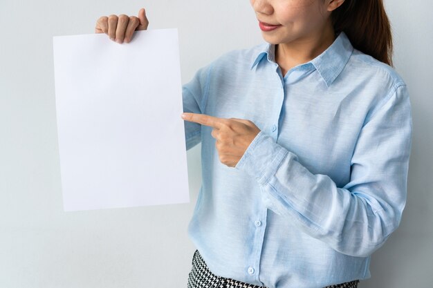 La bella giovane donna asiatica in camicia blu tiene un foglio di carta bianco nelle mani per la pubblicità