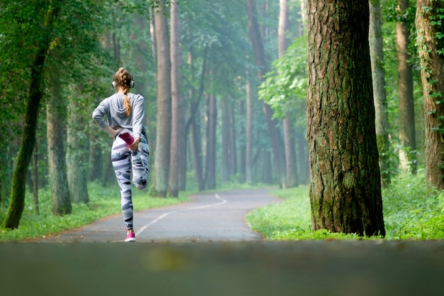 La bella giovane donna attraente che allunga nel parco e ascolta musica